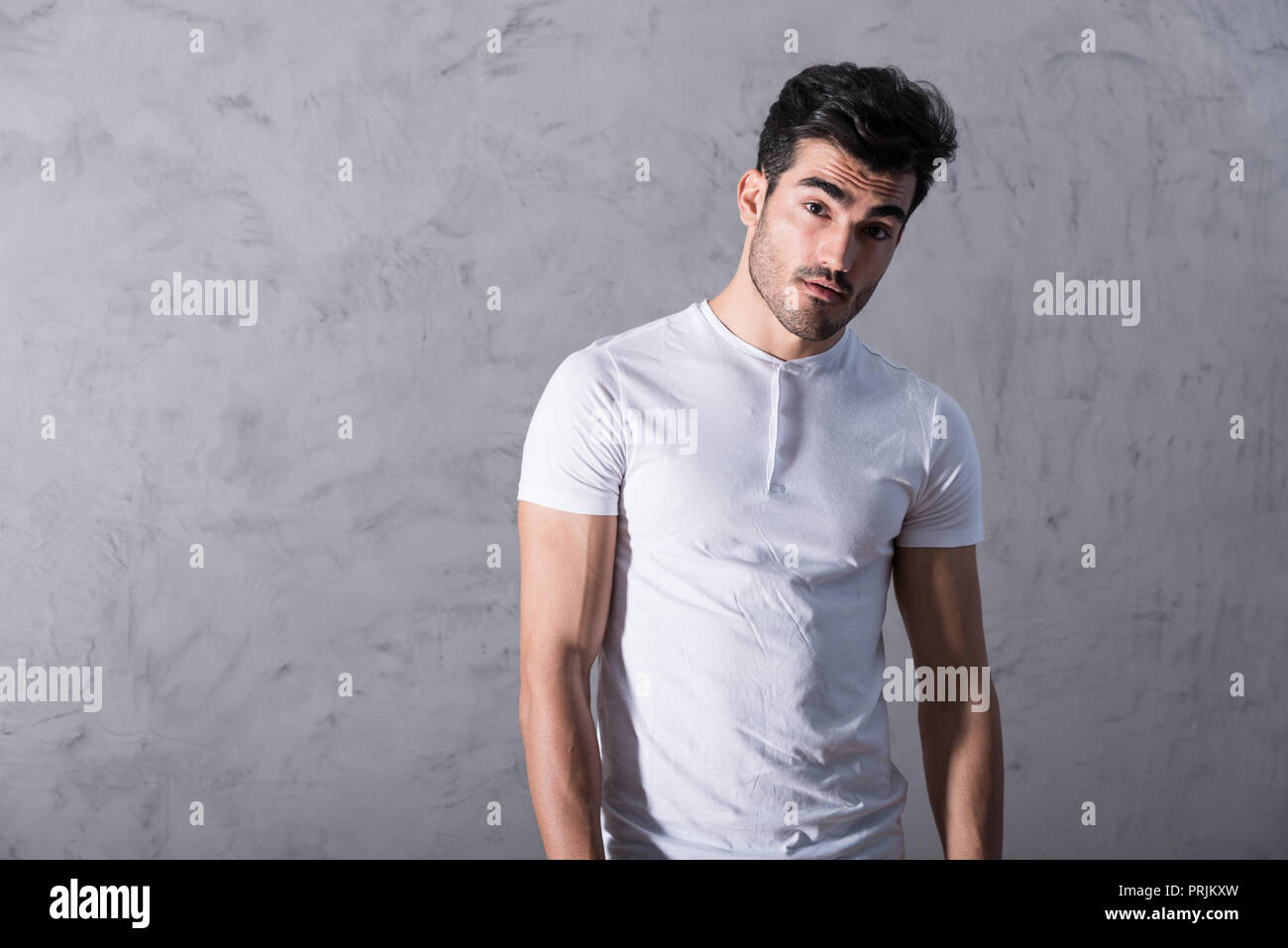 A serious handsome young man in a white tshirt standing in front of a ...