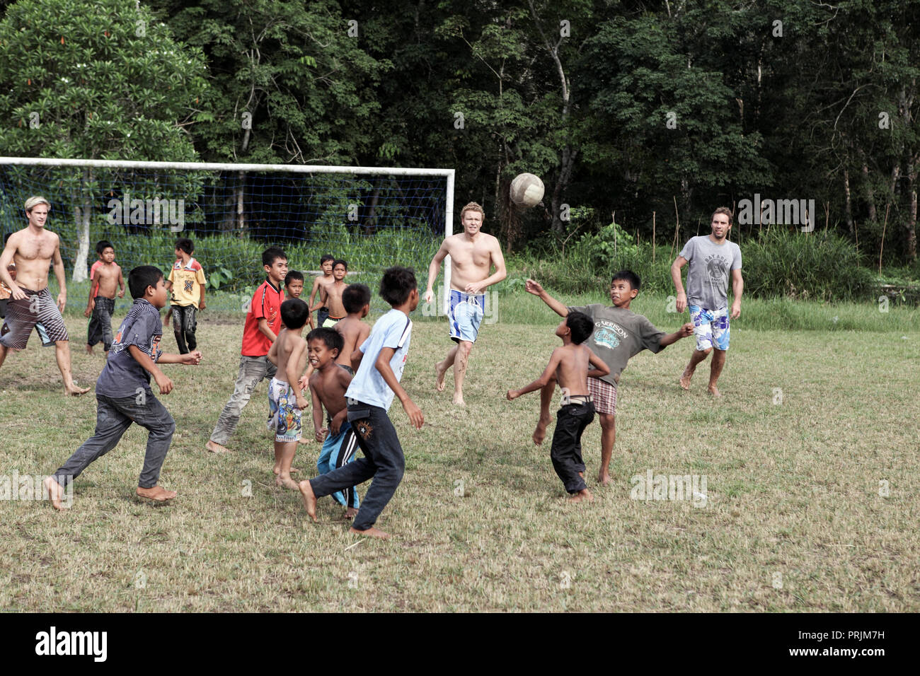 Tourists playing game of football with young local boys at Teluk Meranti village in Sumatra, Indonesia Stock Photo