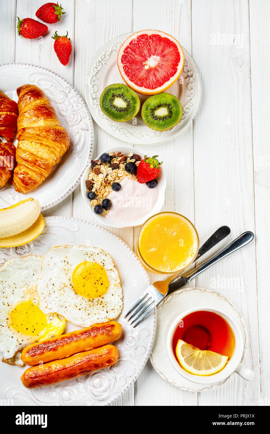 Breakfast of sunny side up eggs, sausages, orange juice, and fruits