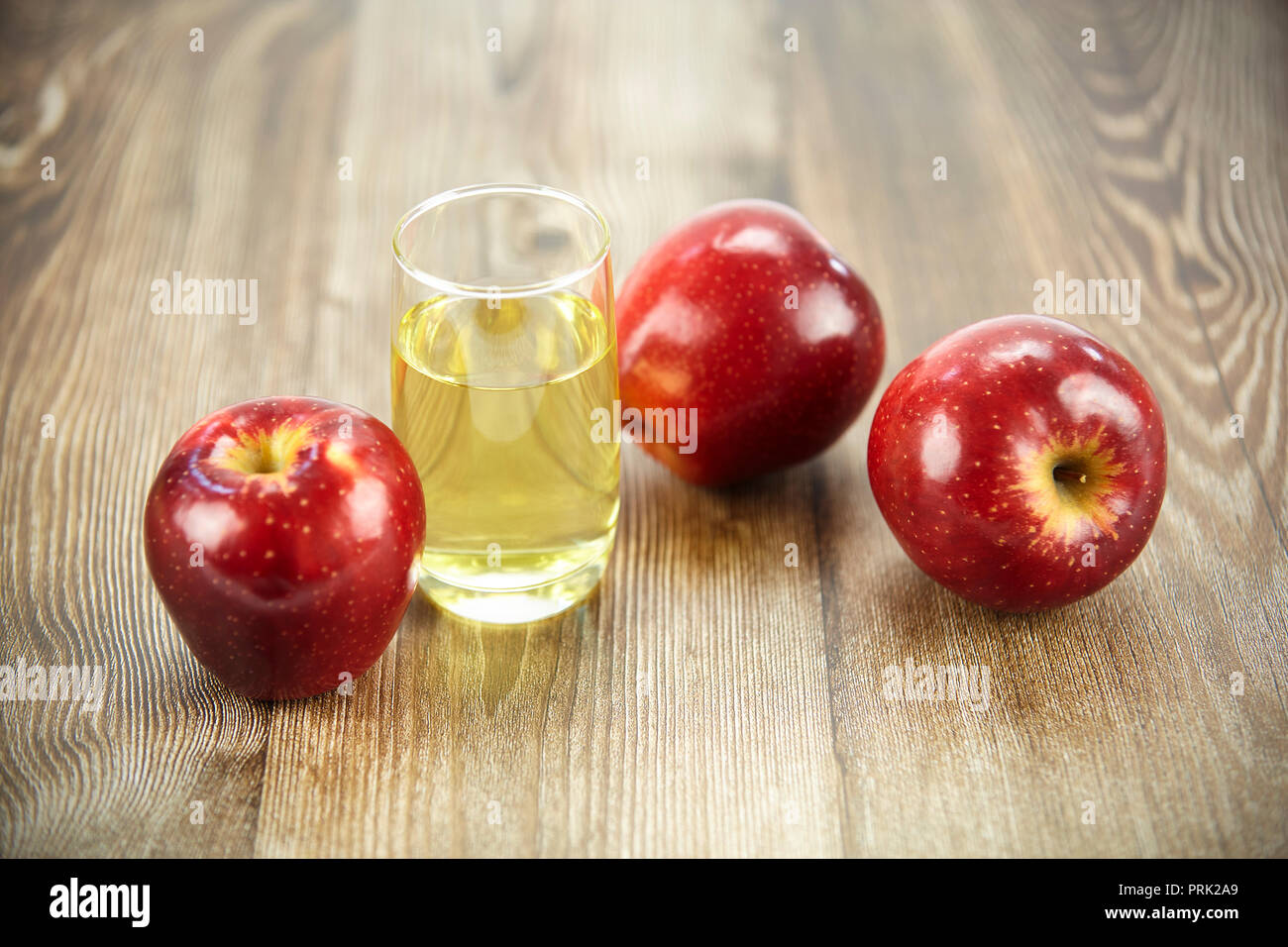 three apples and a glass of apple juice on hard wood surface. Stock Photo