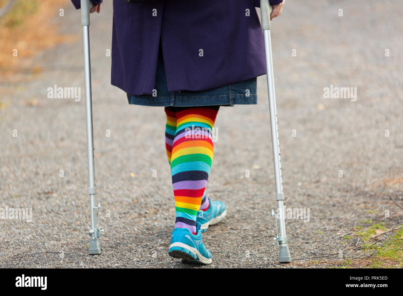 Female with Rainbow Leggings and crutches Walking. Stock Photo