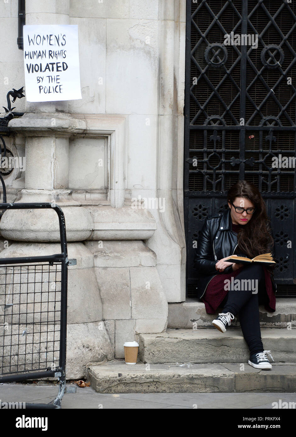 A women reads a book next to a protest sign outside the Royal Courts of Justice, London, where an Investigatory Powers Tribunal is hearing the case of Kate Wilson who was deceived into a relationship by undercover police officer Mark Kennedy. Stock Photo
