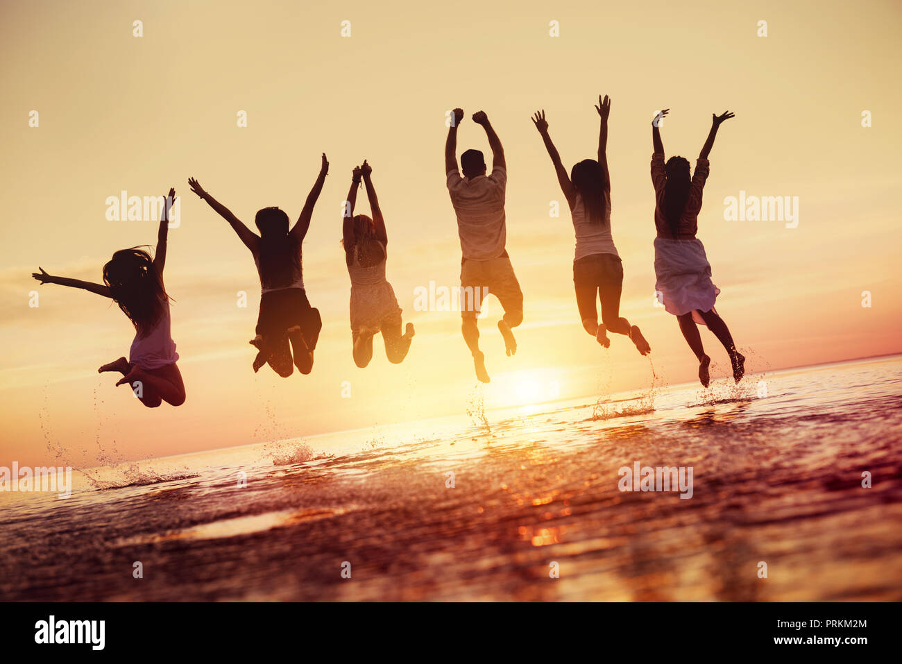 Big group of happy friends having fun and jumps in water against sunset Stock Photo