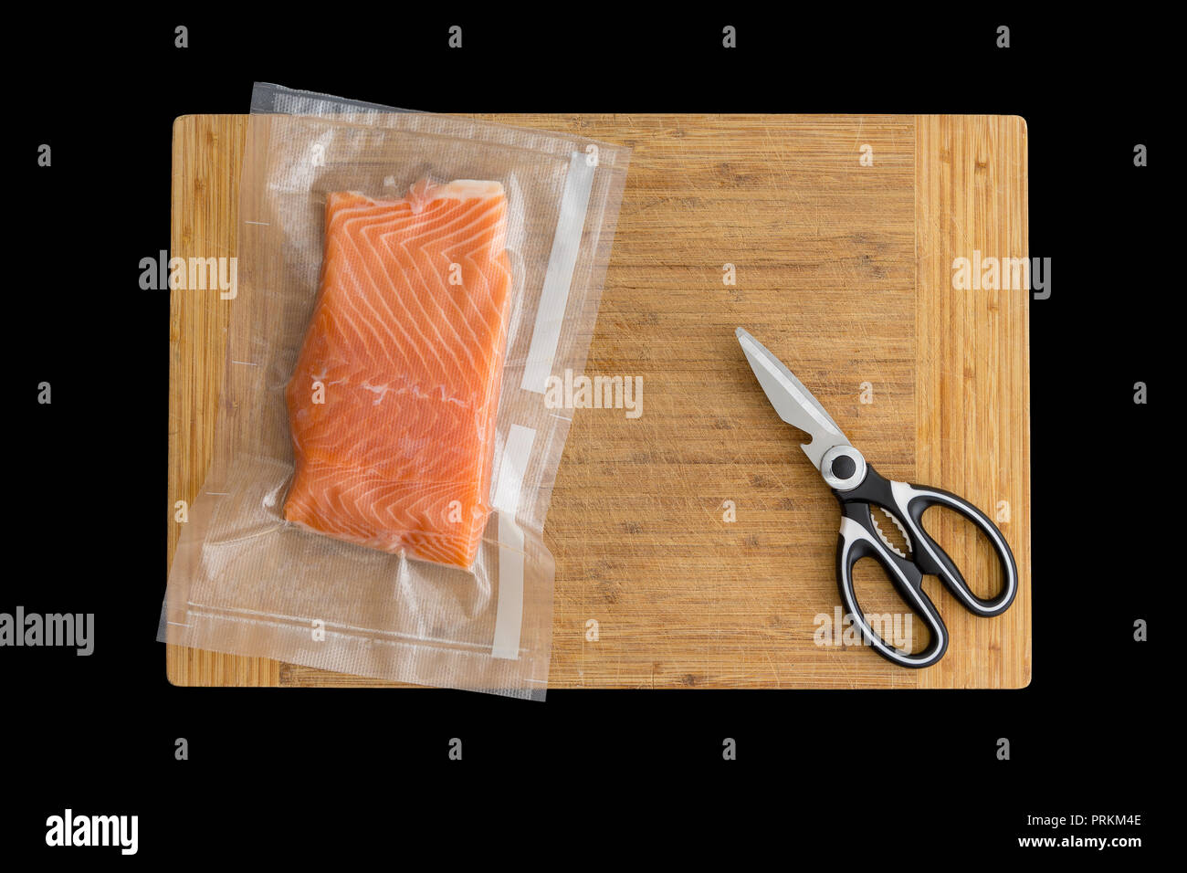 Fillet of fresh Atlantic salmon packaged fro freezing in a vacuum pack of clear plastic lying on a wooden board with scissors viewed from above Stock Photo