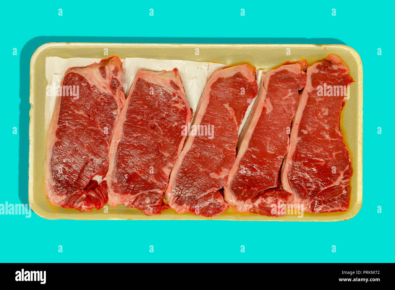 Retail packaging with five raw flat iron steaks , oyster blade steaks or butlers steaks from the shoulder isolated on blue Stock Photo