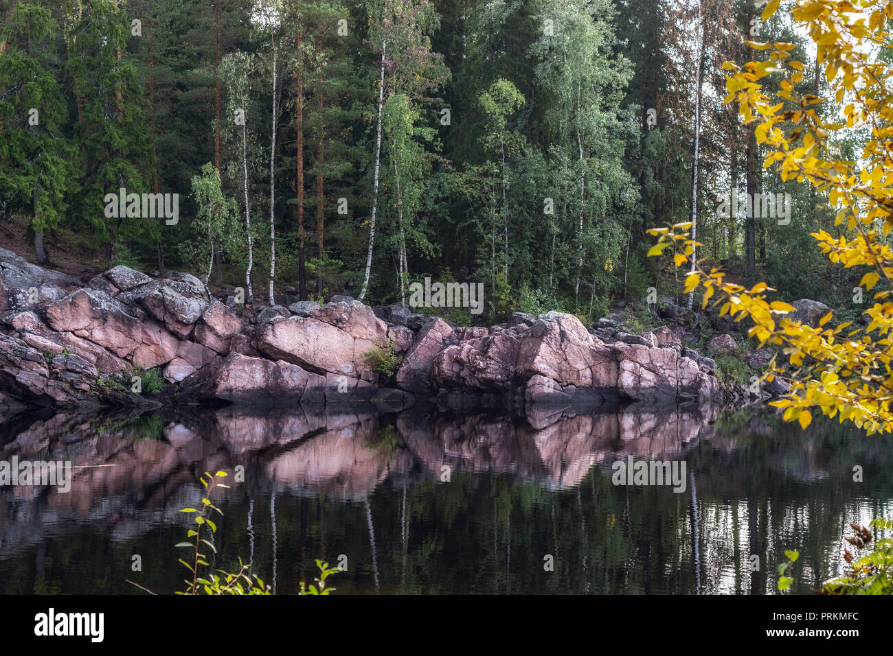 The rocky shore of the river of pink stone reflected on the surface of the water in the Finnish city of Imatra. Stock Photo