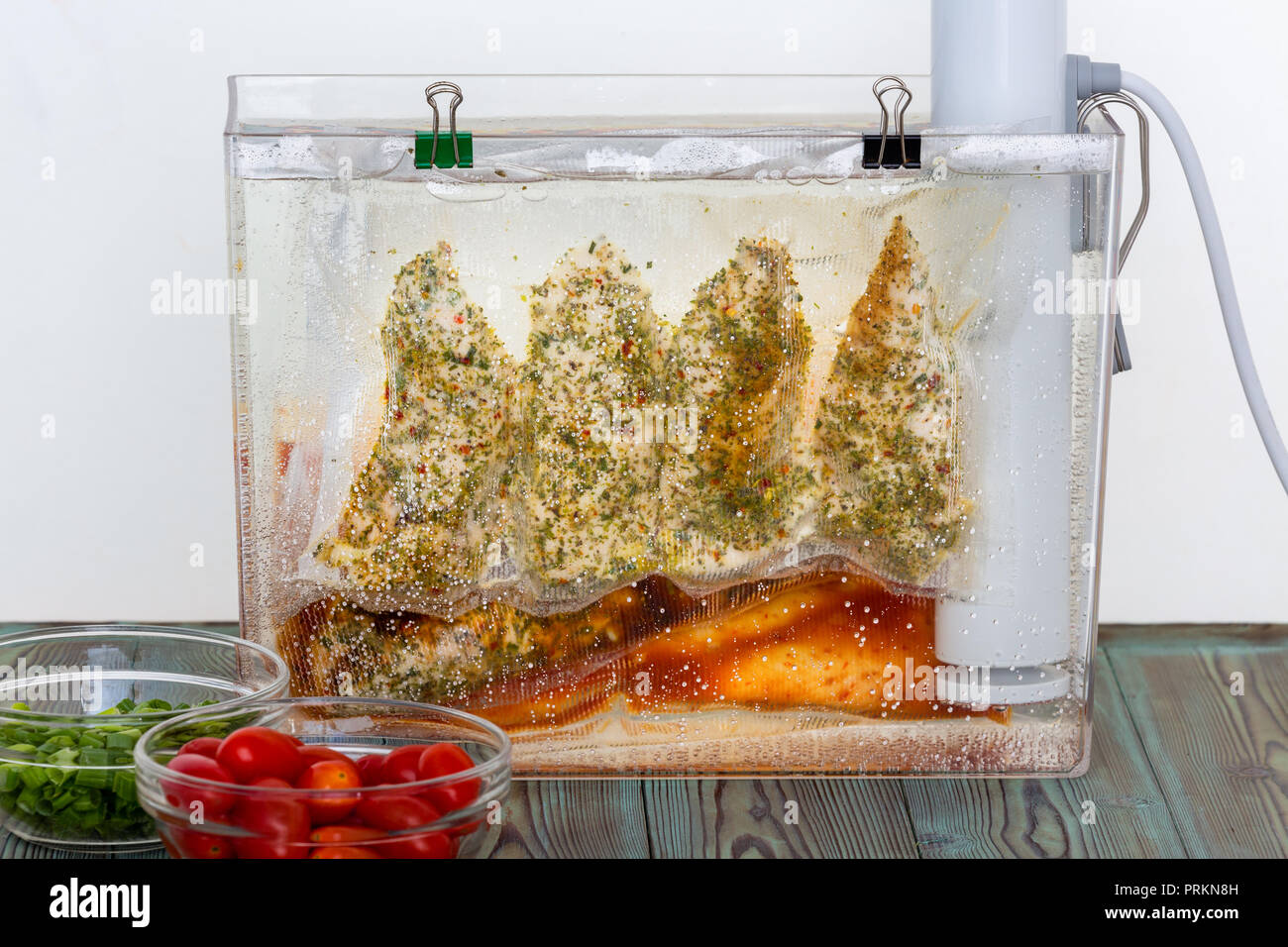 Three bags of chicken breasts with assorted marinades and seasoning hanging suspended in water sous-vide cooking at an even temperature Stock Photo