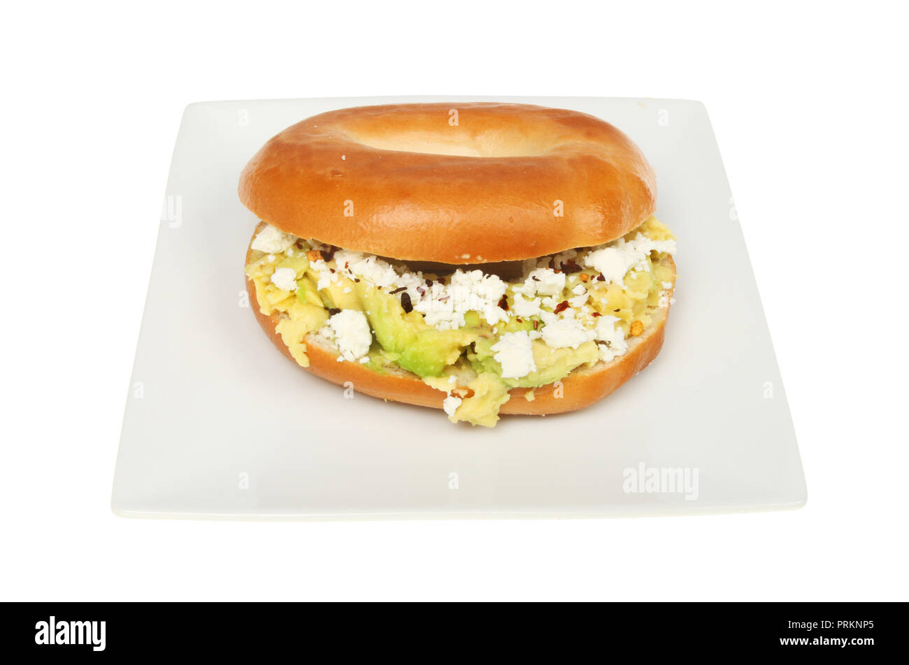 Avocado and feta cheese with chilli flakes in a bagel on a plate isolated against white Stock Photo