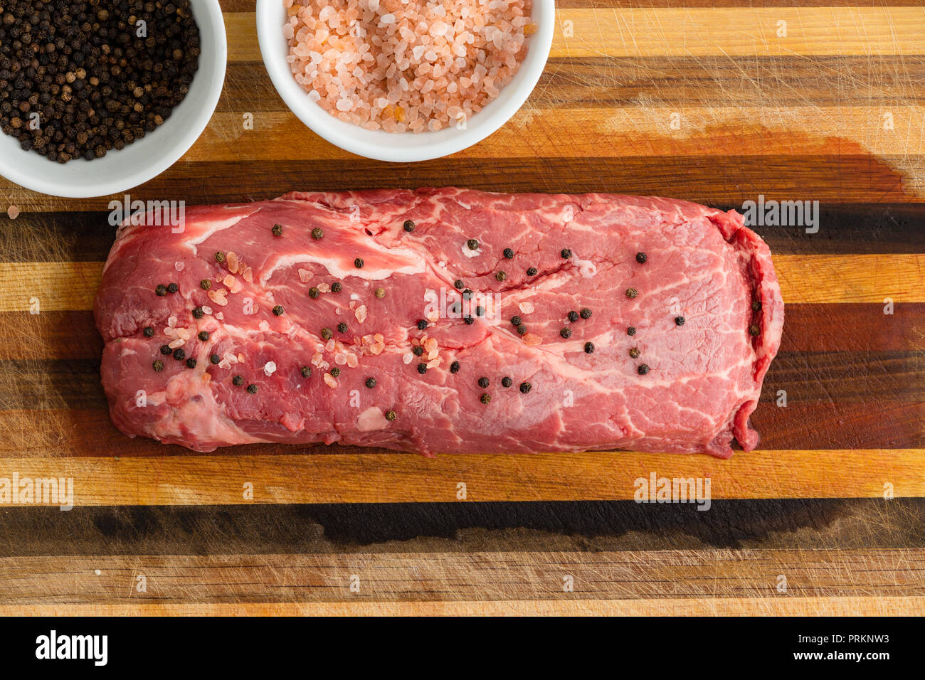 Rectangular slice of steak covered with tiny balls of pepper sitting on table next to bowls of seasoning Stock Photo