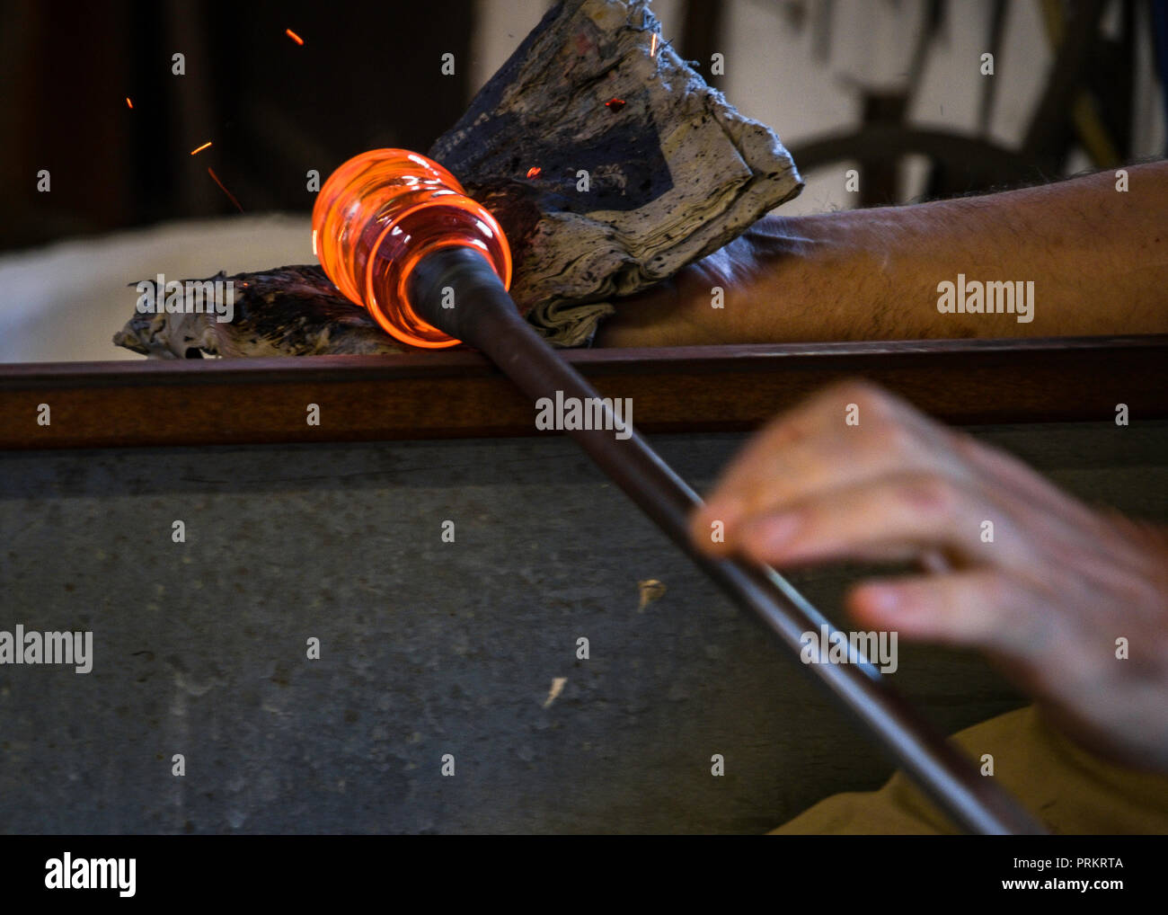 A glassblower uses a pad on a blob of molten glass to form a shape. Stock Photo