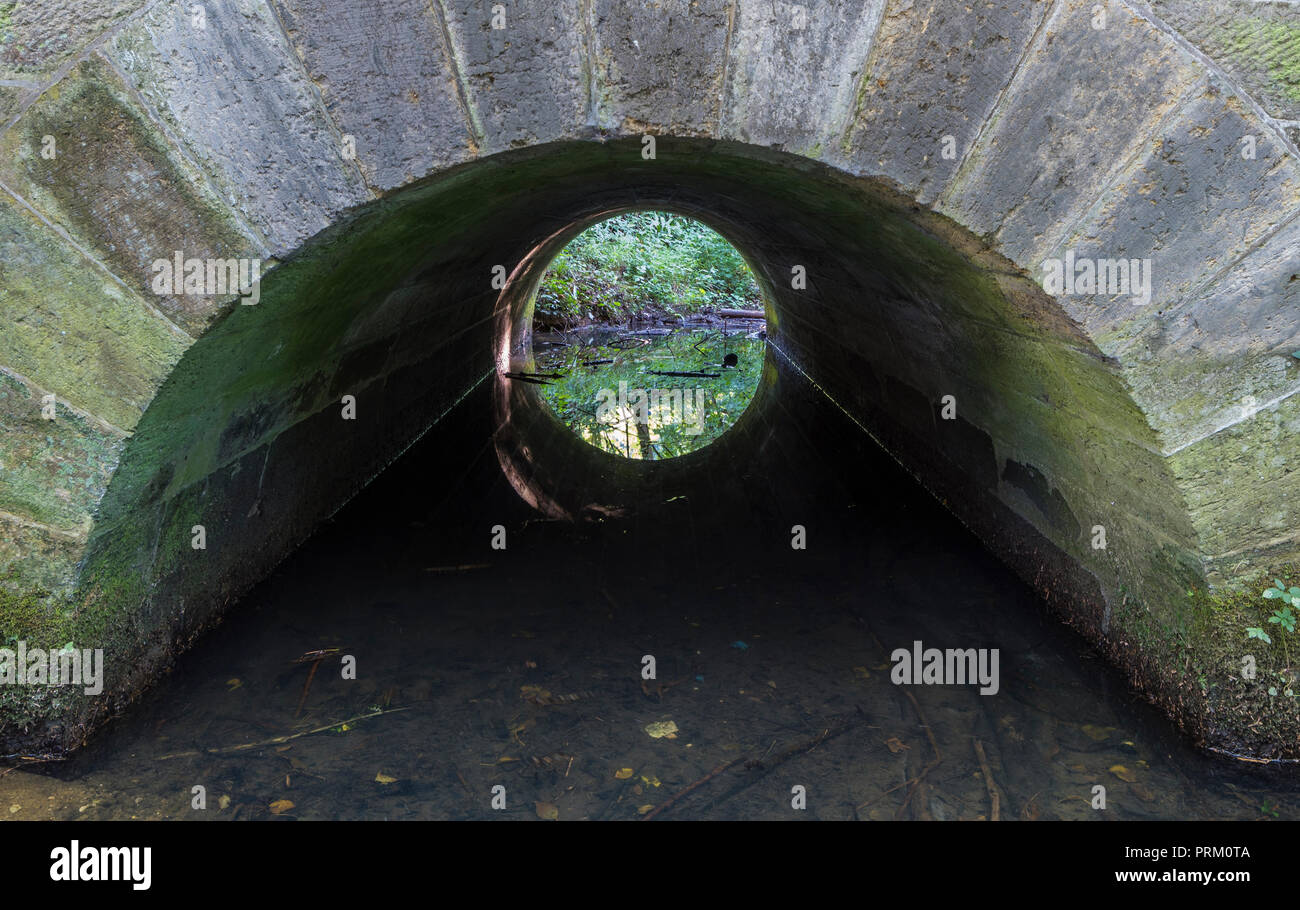 Narrow stone arched tunnel under a bridge with water running through it. Stock Photo