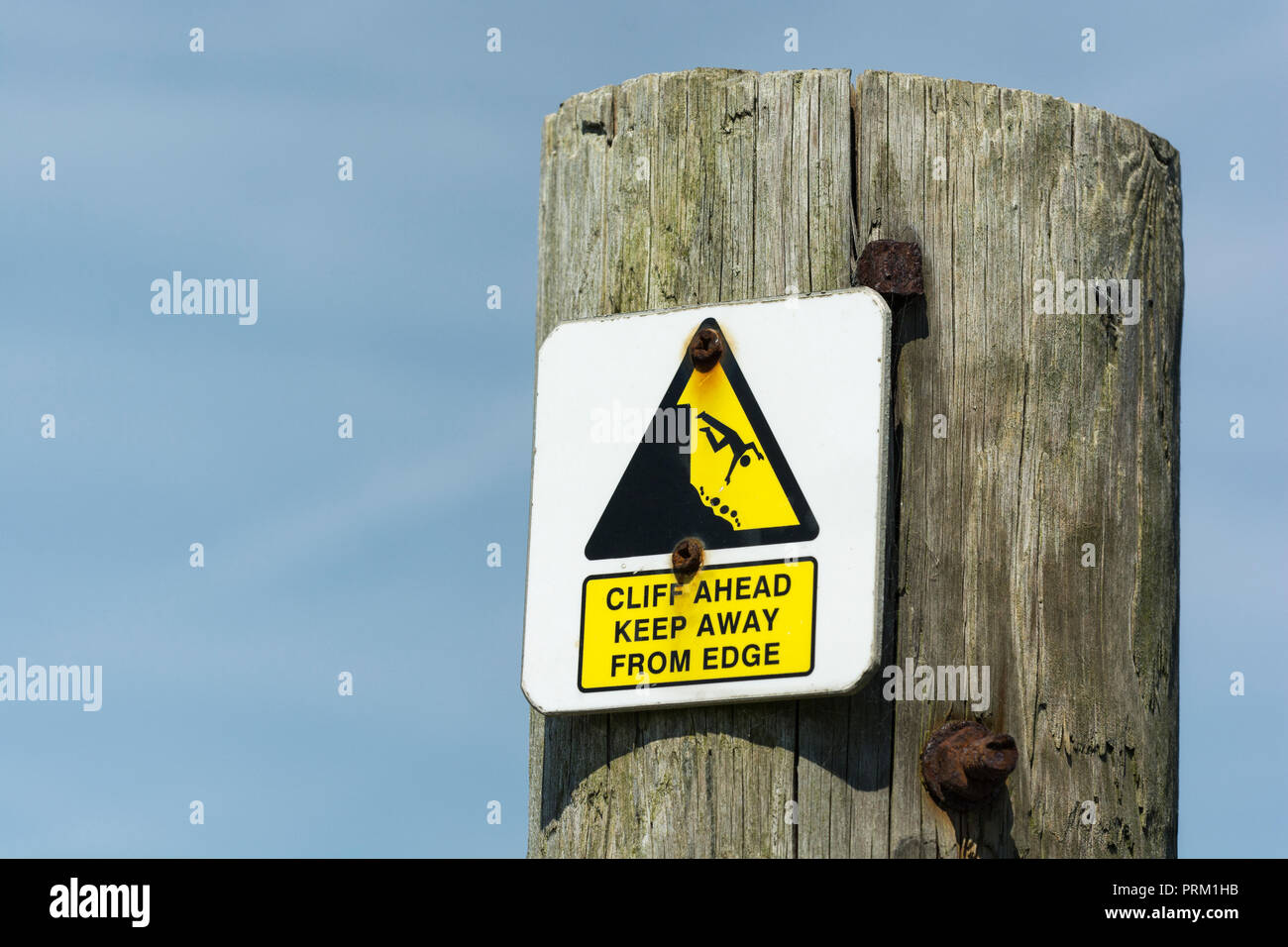 Warning yellow triangle sign highlighting dangerous cliff edge nearby. Keep away from the edge concept, falling off, falling man pictogram. Stock Photo