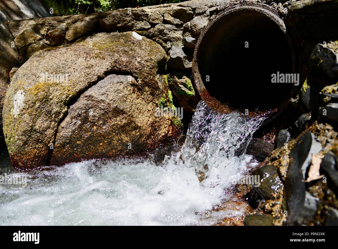 Clear water from a mountain stream flowing through a concrete pipe