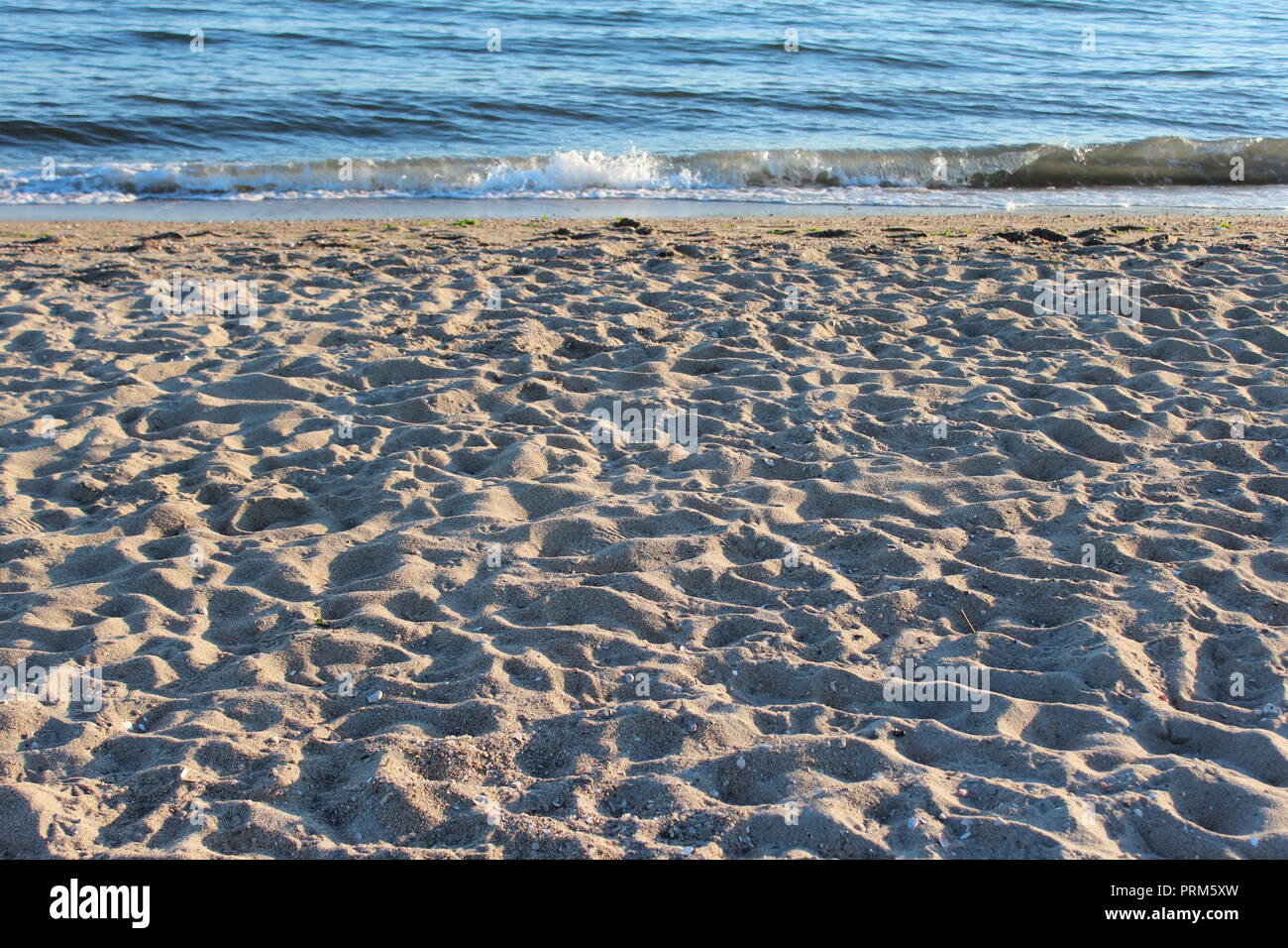 Beach with many footprints from a happy day by the shoreline.  Waves still gently lapping on the shore. Stock Photo