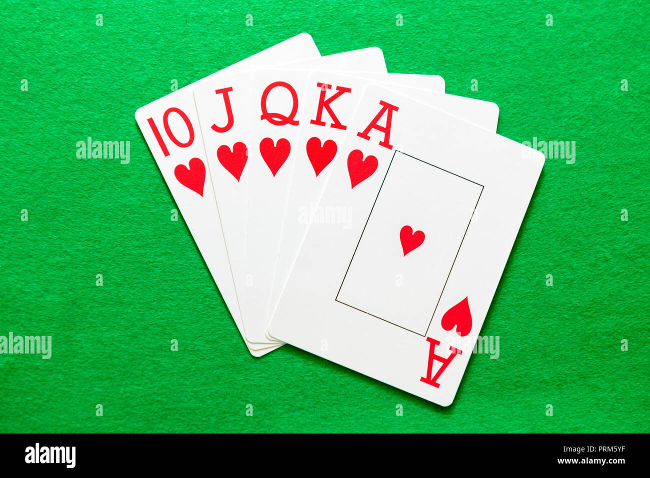 Royal Flush Hearts, a winning hand in a game of poker. Playing cards on a green baize table. Stock Photo