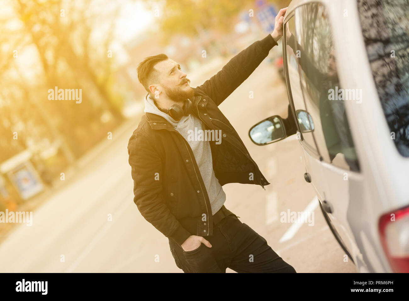A handsome young hipster man standing next to his car and waiting. Stock Photo