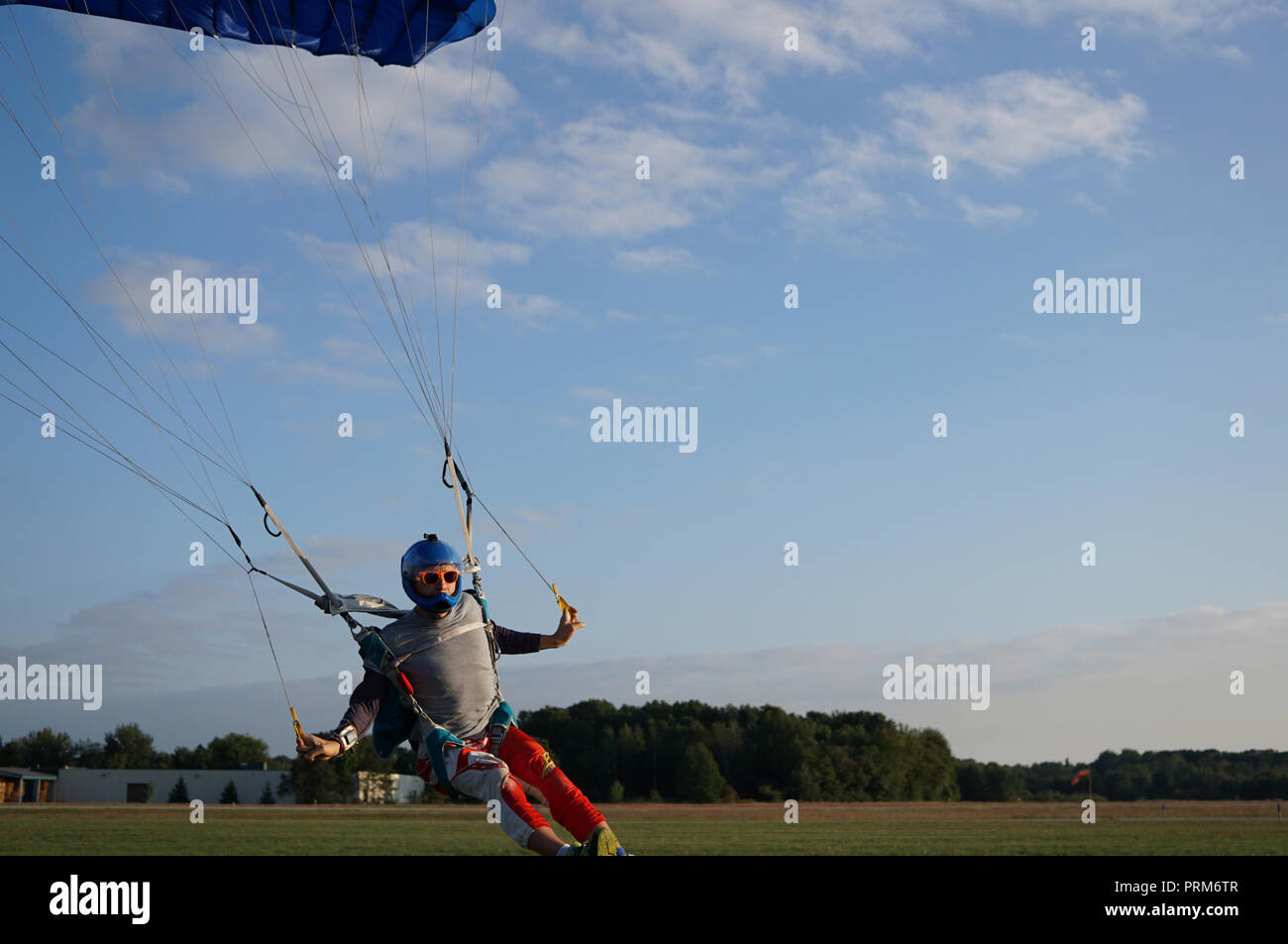 Skydiver under a dark blue little canopy of a parachute is landing on
