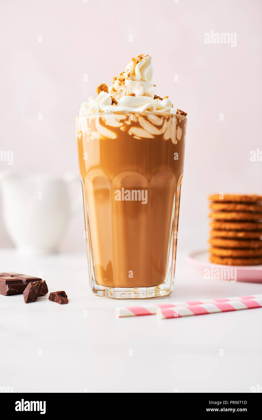 Chocolate ice coffee with whipped cream and cookies in a tall glass with pink straws on white marble table over rose background. High resolution image Stock Photo