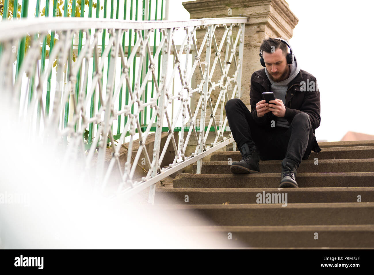 A handsome young hipster man sitting on the stairs and checking his ...