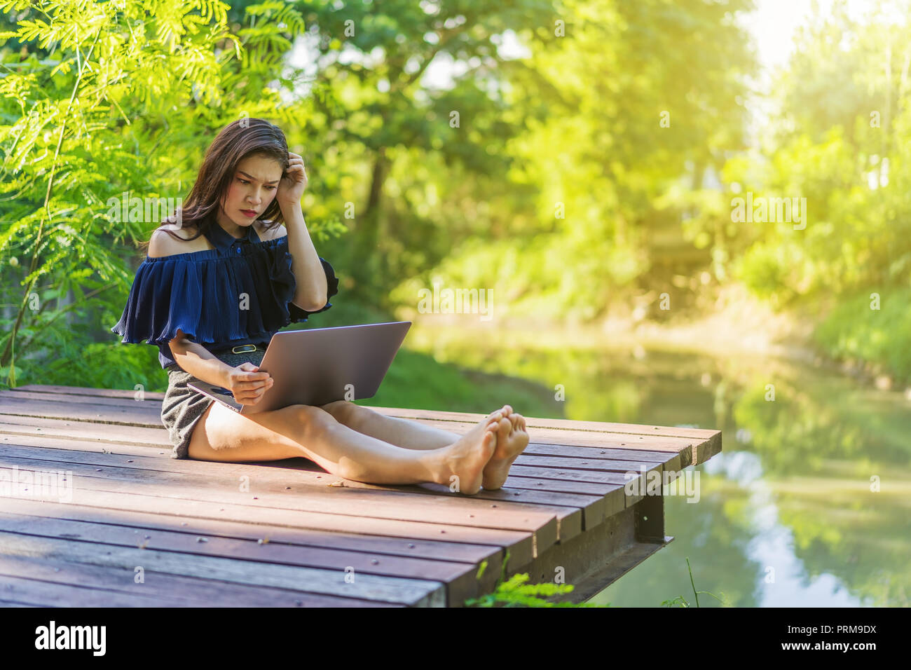 stressed woman using laptop computer on a wooden jetty Stock Photo
