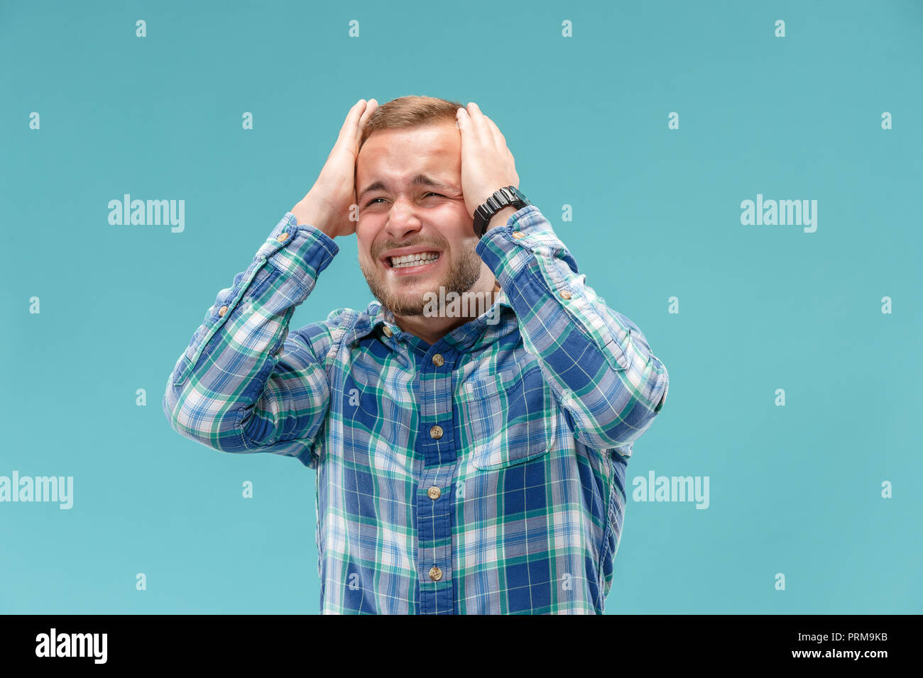 Horrible, stress, shock. Male halflength portrait isolated at blue studio. Young emotional