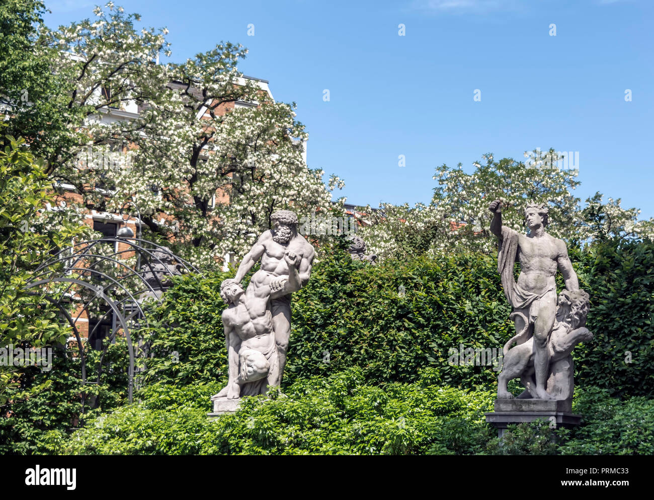 Two antique sculptures in the Rijksmuseum (National Museum) gardens among blossoming spring trees. Stock Photo