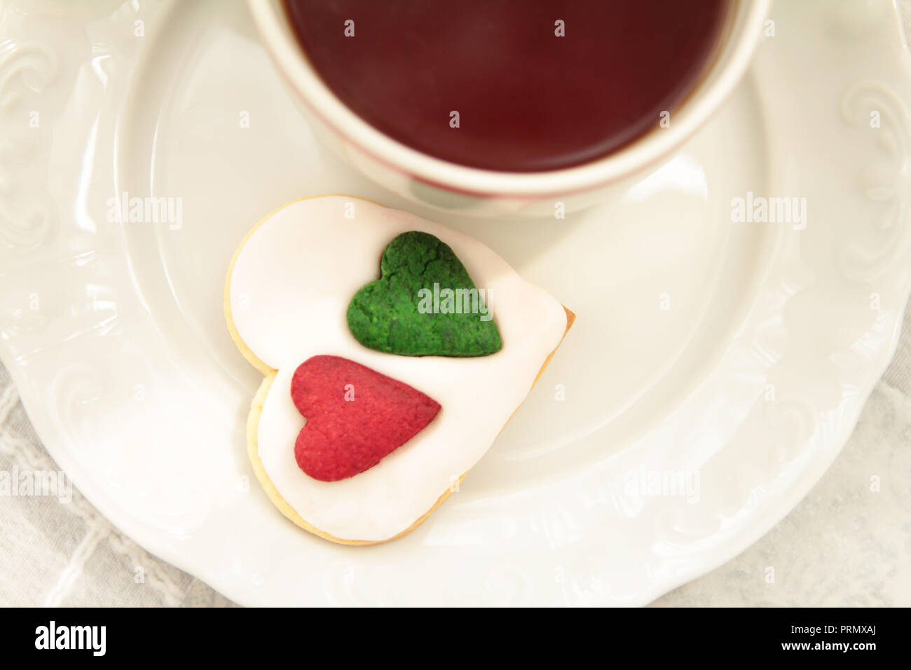 Porcelain cup of tea and sweet homemade heart shape cookies on cloth surface close up  cropped view, selective focus Stock Photo