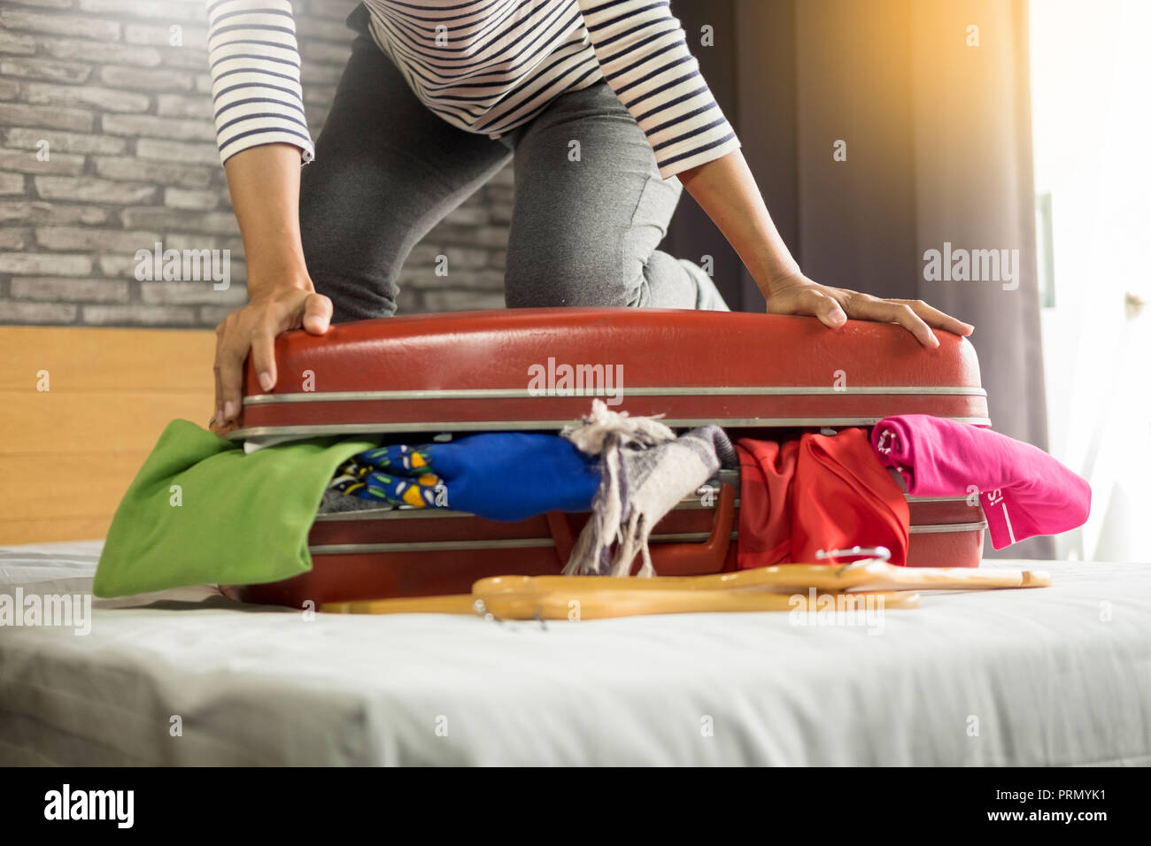 Woman trying to fit all clothing to packing her red suitcase before
