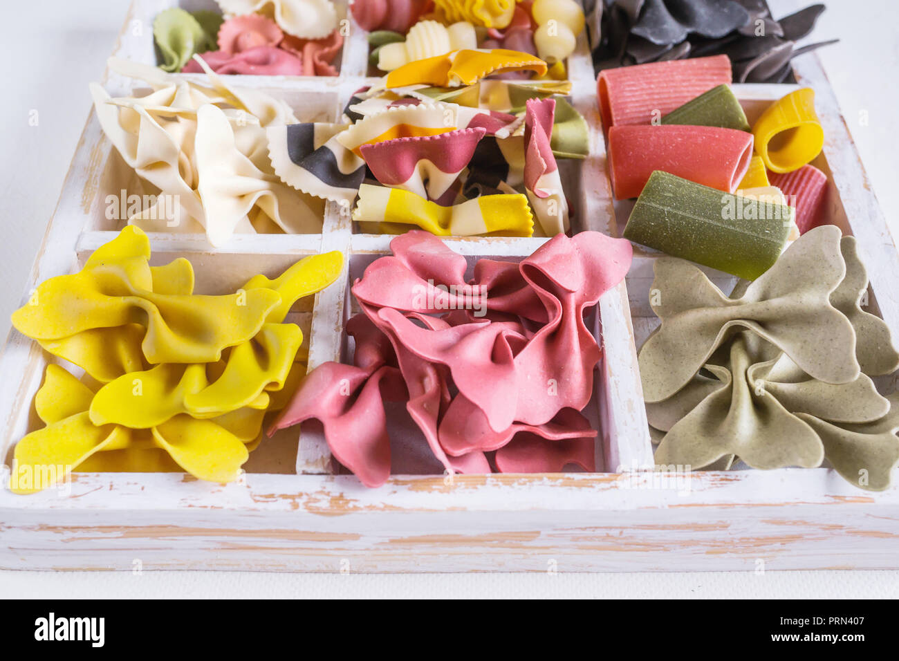 Mixed set of dry multi-colored Italian pasta on a white old wooden box. Background. Close up. Stock Photo