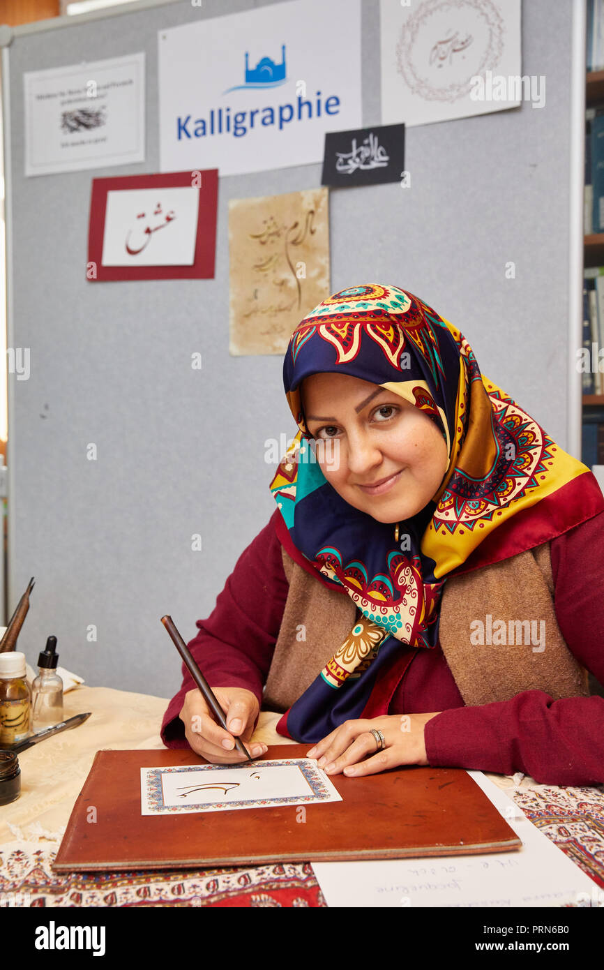 03 October 2018, Hamburg: Zeinab Eskandarian, Persian calligrapher, writes a name for a visitor at her stand on Open Mosque Day in the Islamic Academy. Photo: Georg Wendt/dpa Stock Photo