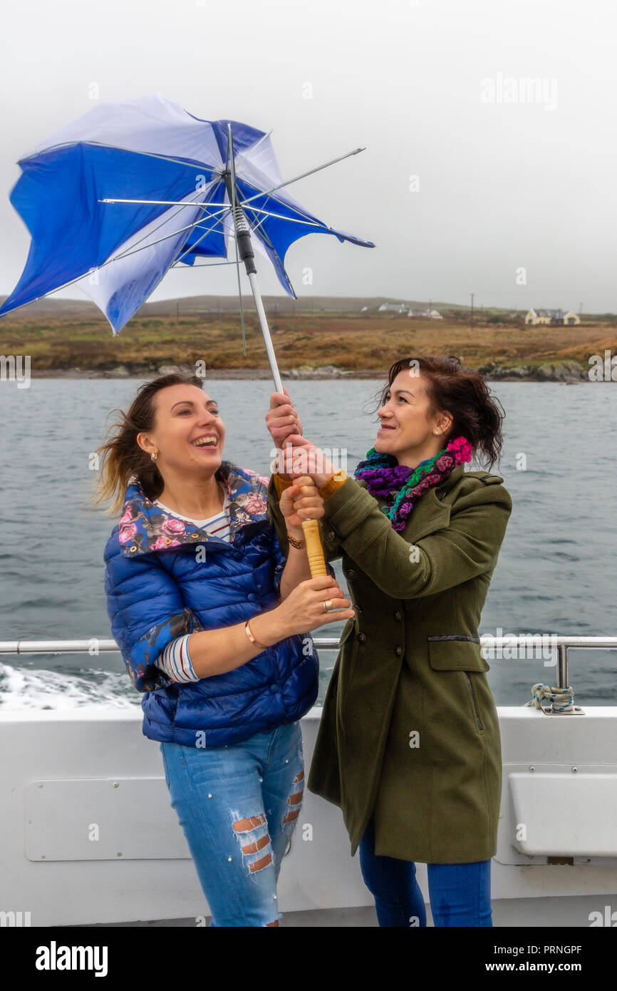 Two young women with broken umbrella on a windy day in County Kerry Ireland Stock Photo