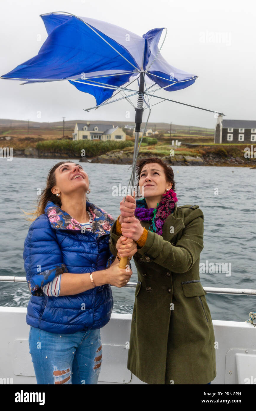 Two young women with broken umbrella on a windy day in County Kerry Ireland Stock Photo