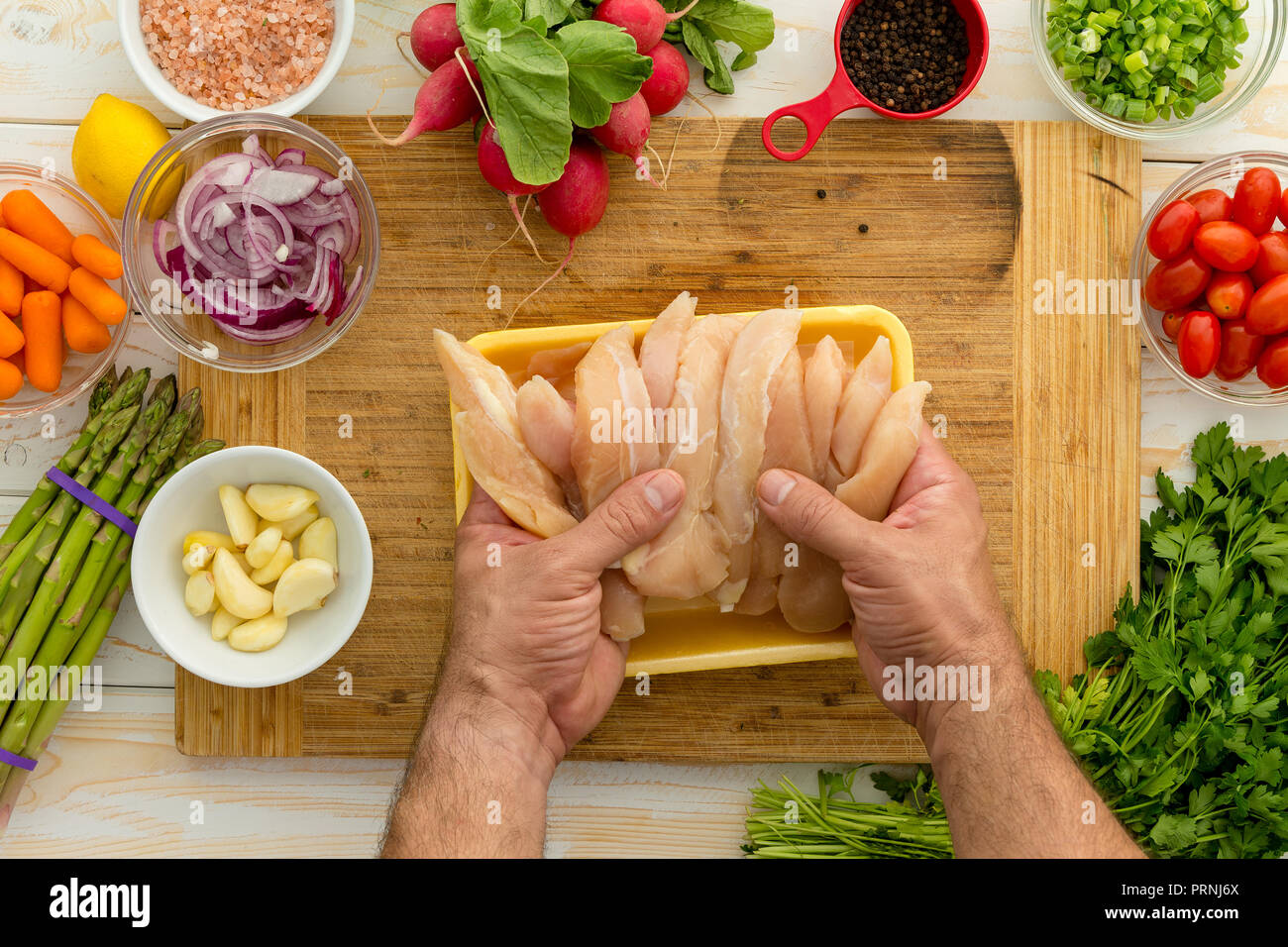 Chef preparing chicken strips with vegetables and seasonings on cutting board for dinner perhaps lunch Stock Photo