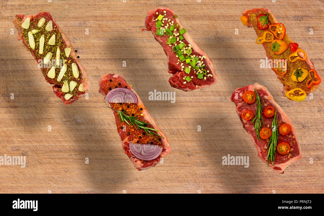 Conceptual floating view of five New York Strips on cutting board seasoned with colorful vegetables with copy space Stock Photo