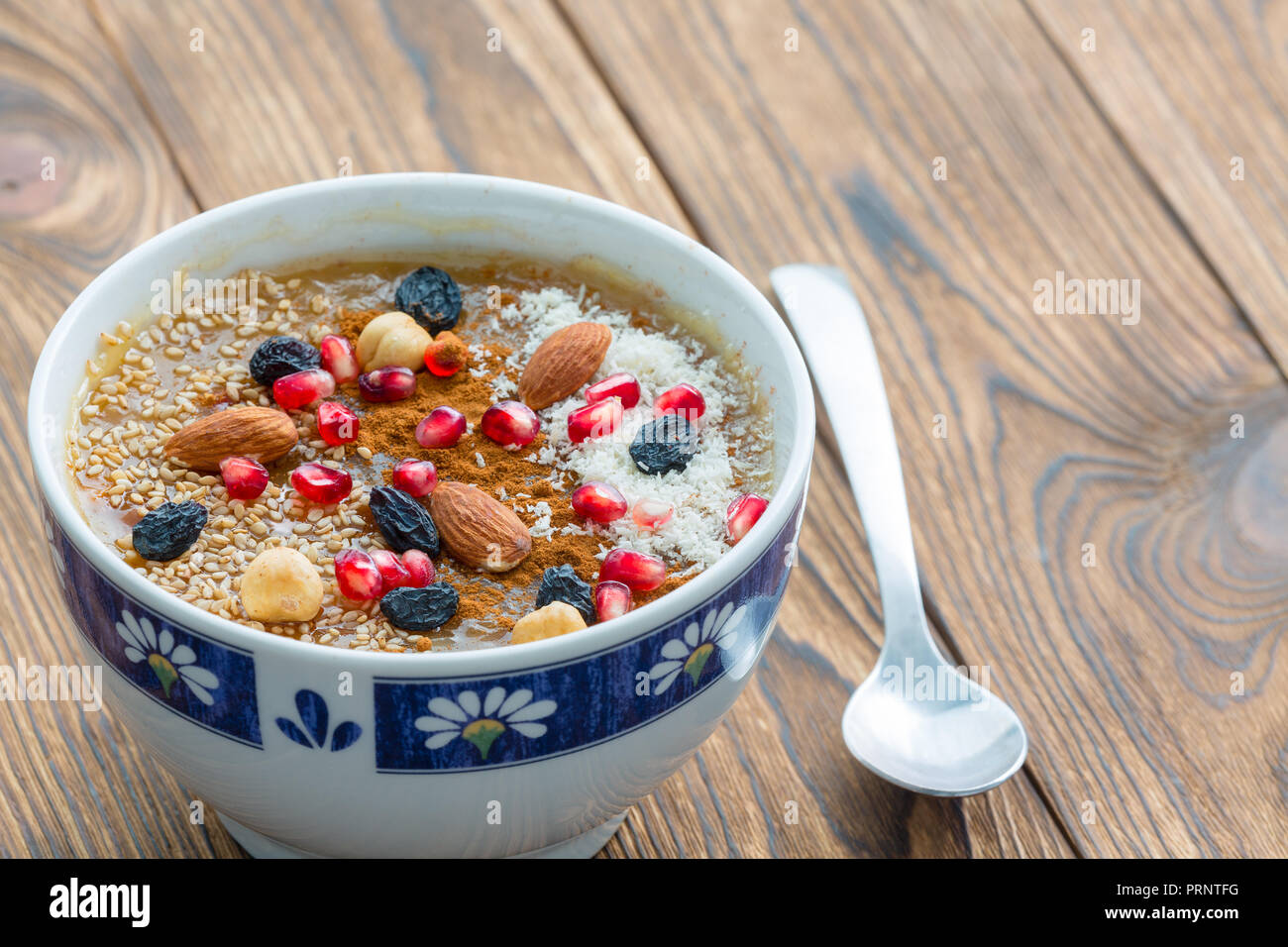 Small asure bowl of tasty cereal with nuts and fruit next to small spoon sitting on brown wood plank table Stock Photo