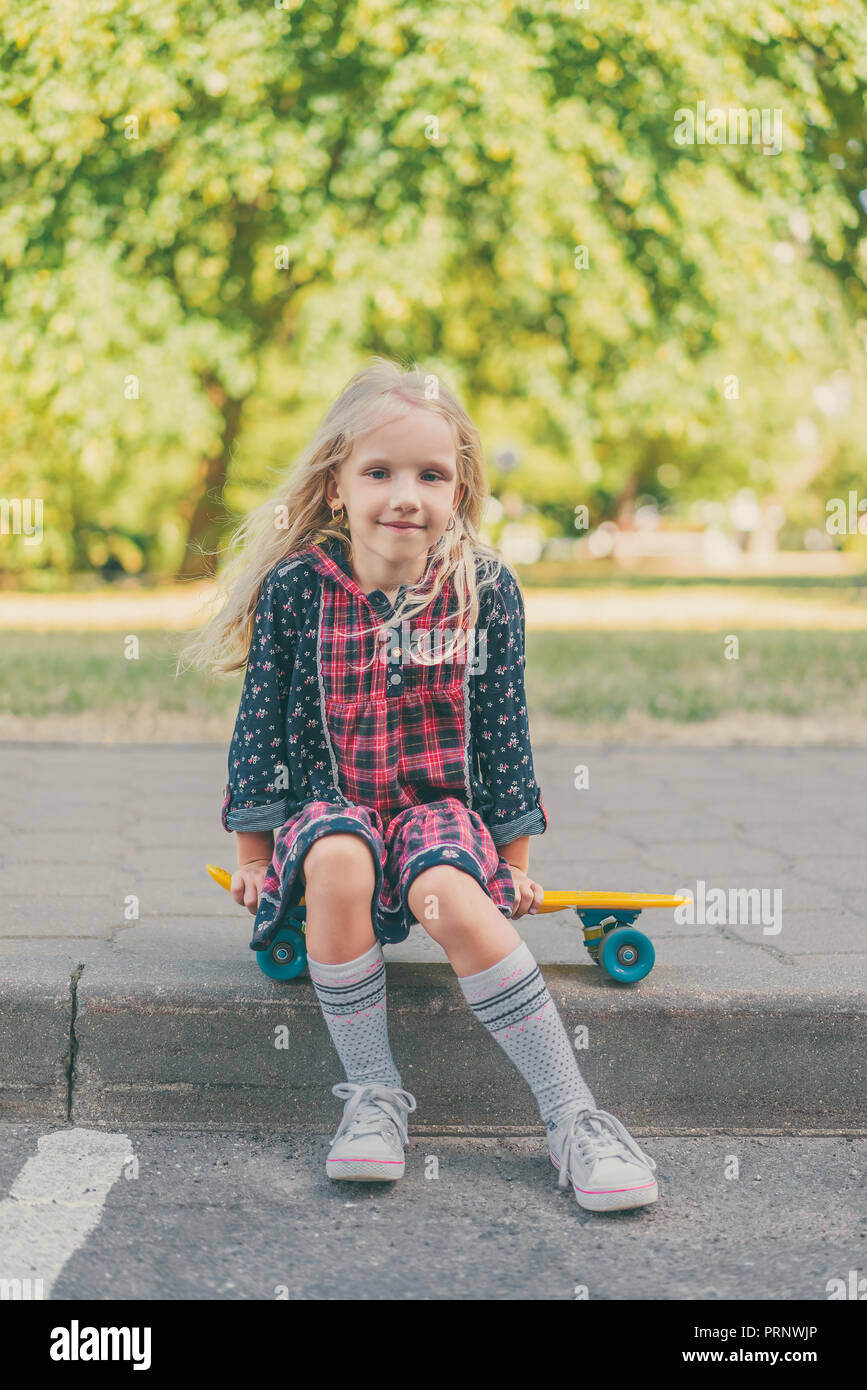 happy child sitting on skateboard and looking at camera at urban street Stock Photo