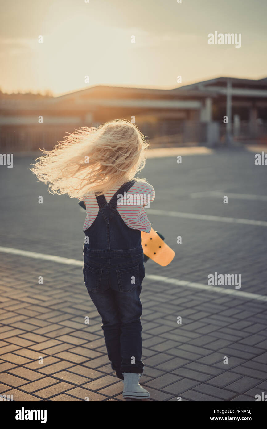 rear view of little kid running with skateboard at parking lot Stock ...
