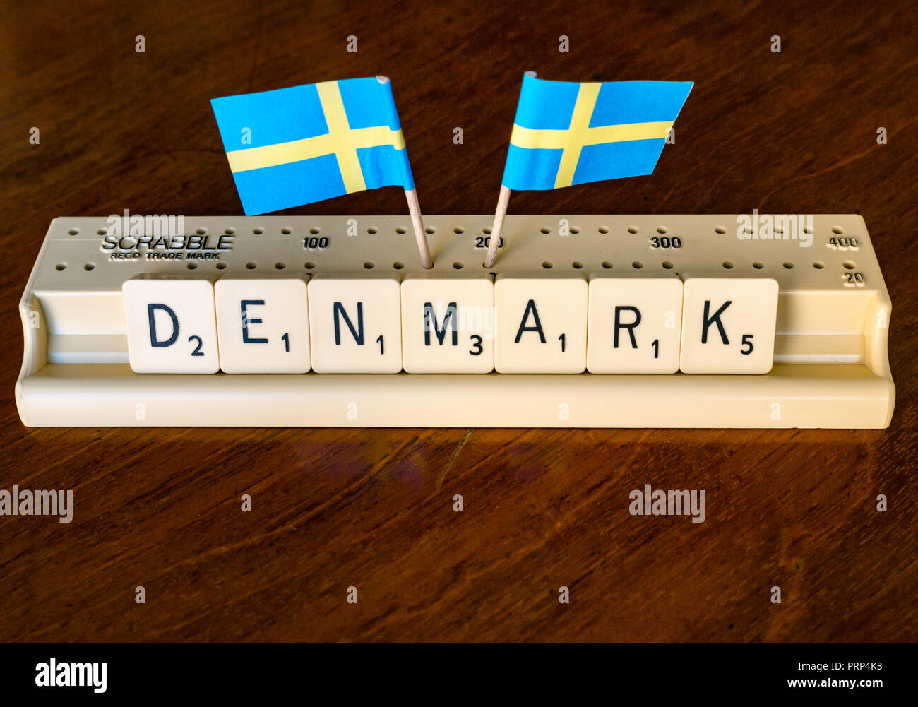 Scrabble letters spelling Denmark in Scrabble tray with Danish flags on dark mahogany background Stock Photo