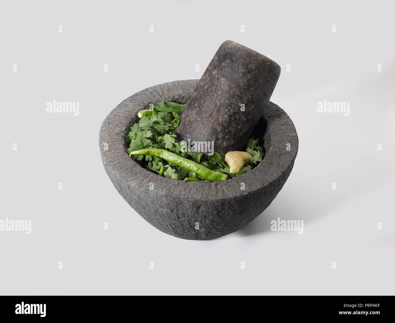 Stone grinder and pestle with coriander, green pepper ginger and mint on a white background Stock Photo