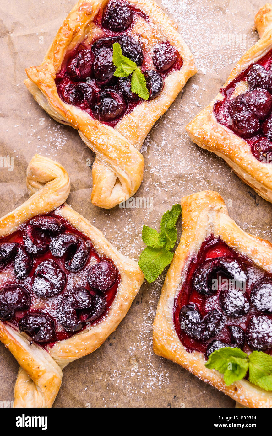 Homemade puff pastry with cherry. Sweet tasty dessert. Decorated with mint leaves. On parchment paper. Stock Photo