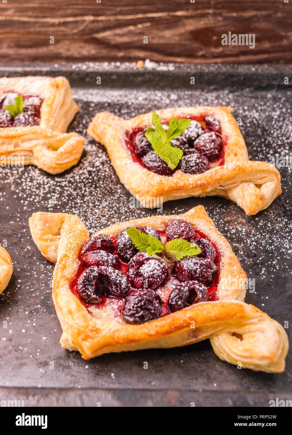 Homemade puff pastry with cherry. Sweet tasty dessert. Decorated with mint leaves. On old black cooking sheet. Stock Photo