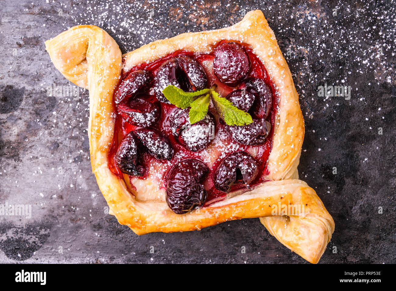 Homemade puff pastry with cherry. Sweet tasty dessert. Decorated with mint leaves. On old black cooking sheet. Stock Photo