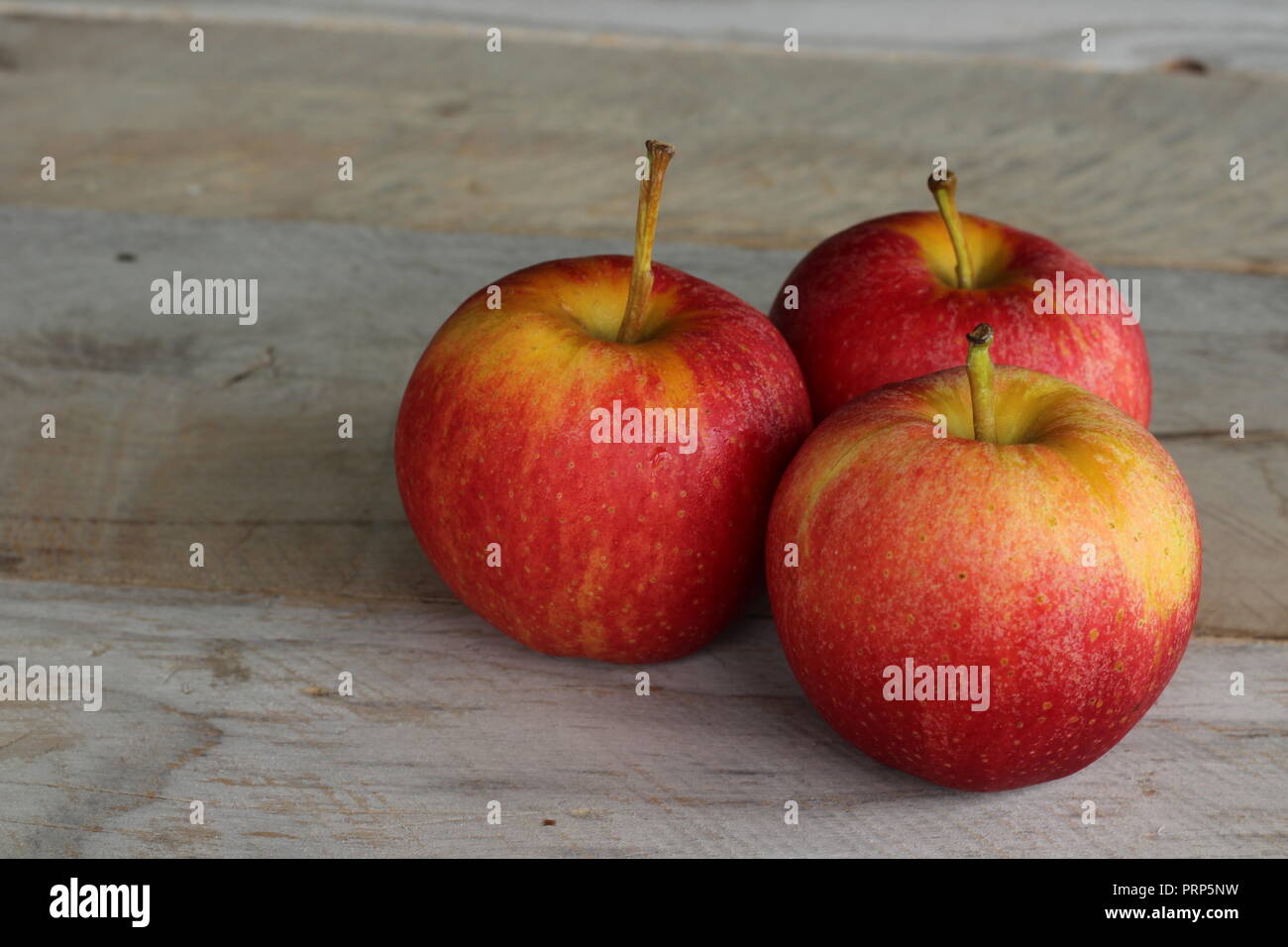 Three ripe apples sitting on a wood board Stock Photo