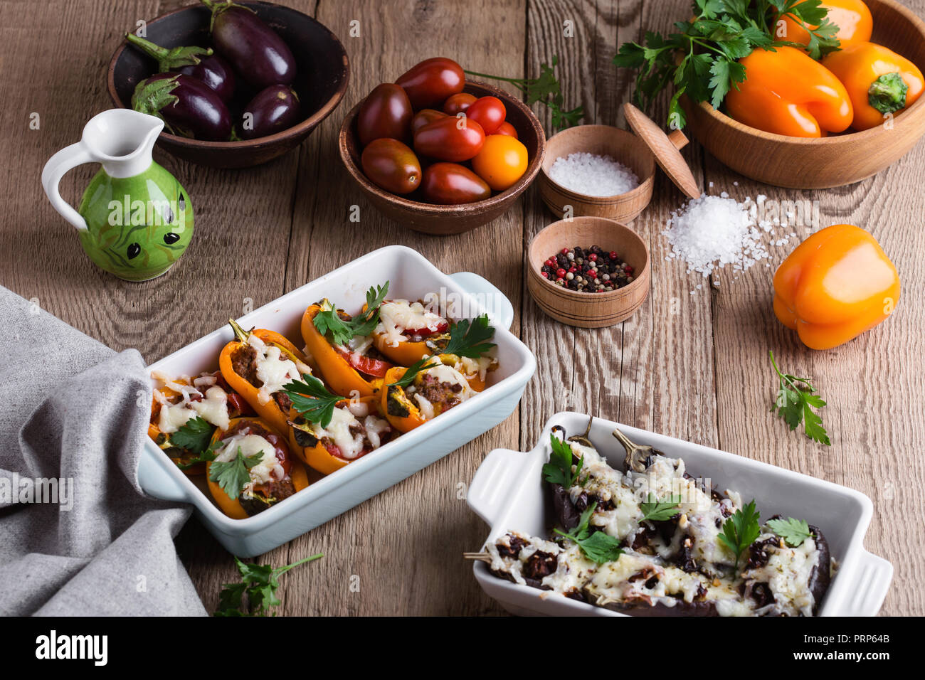 Stuffed eggplants with sun dried tomatoes, bell peppers with minced meat, baked vegetables with mozzarella cheese on top in ceramic dishes on rustic Stock Photo