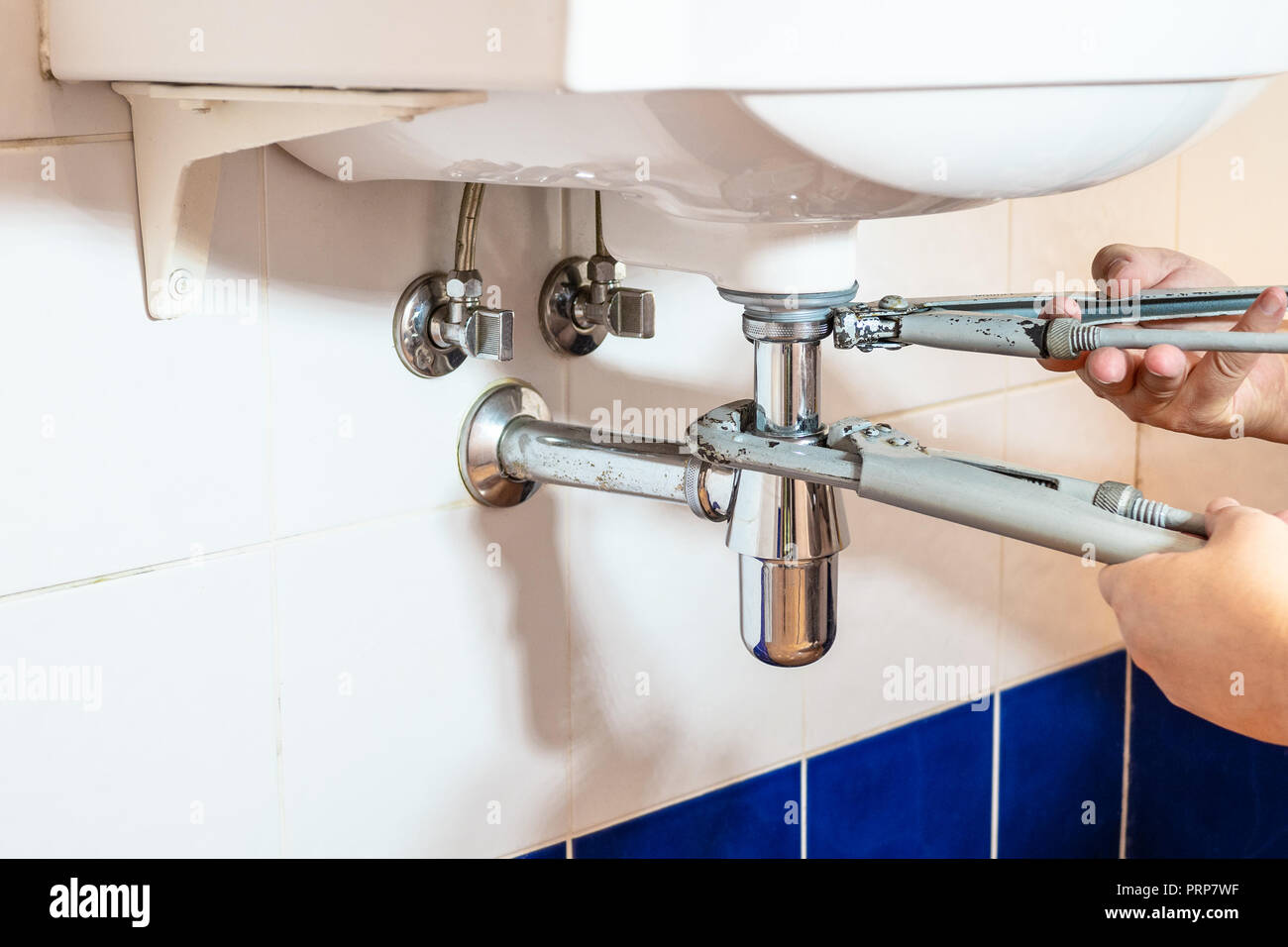 plumber fixes sink siphon by two pipe-wrenches in bathroom Stock Photo