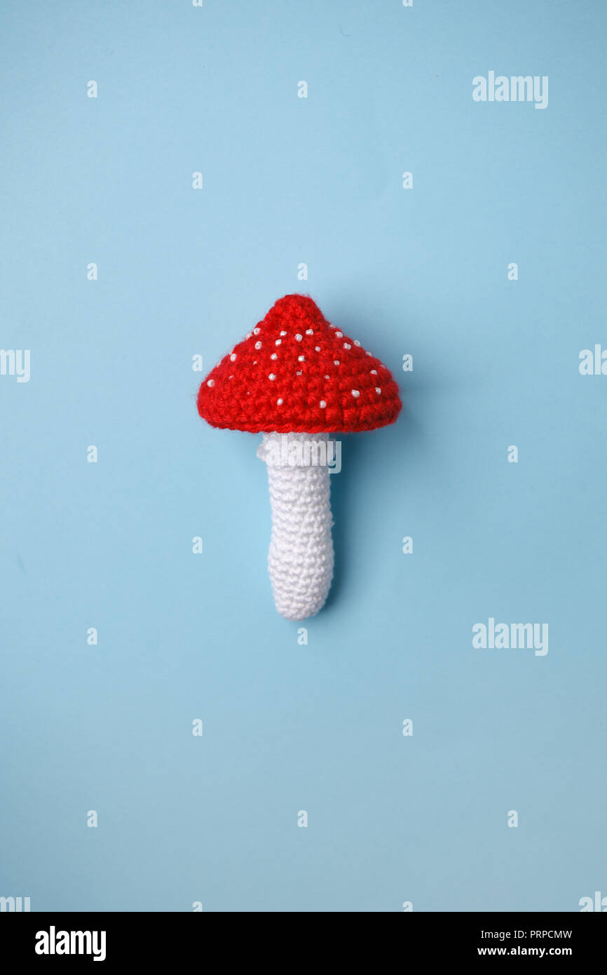 knitted toy amanita on blue background. Earlier tactile development of children, craft toys, poisonous food Stock Photo