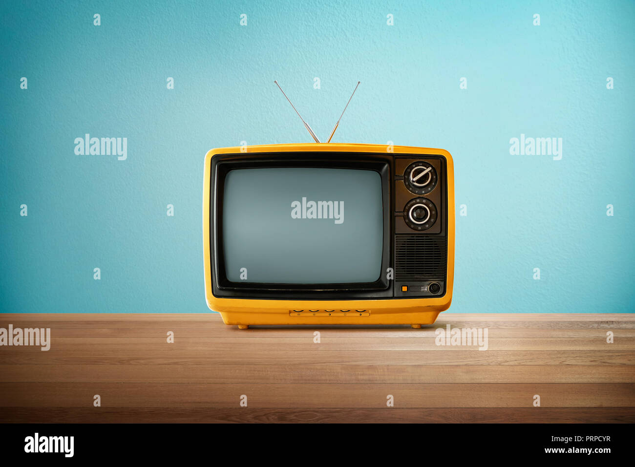 Yellow Orange color old vintage retro Television on wood table with mint blue background . Stock Photo