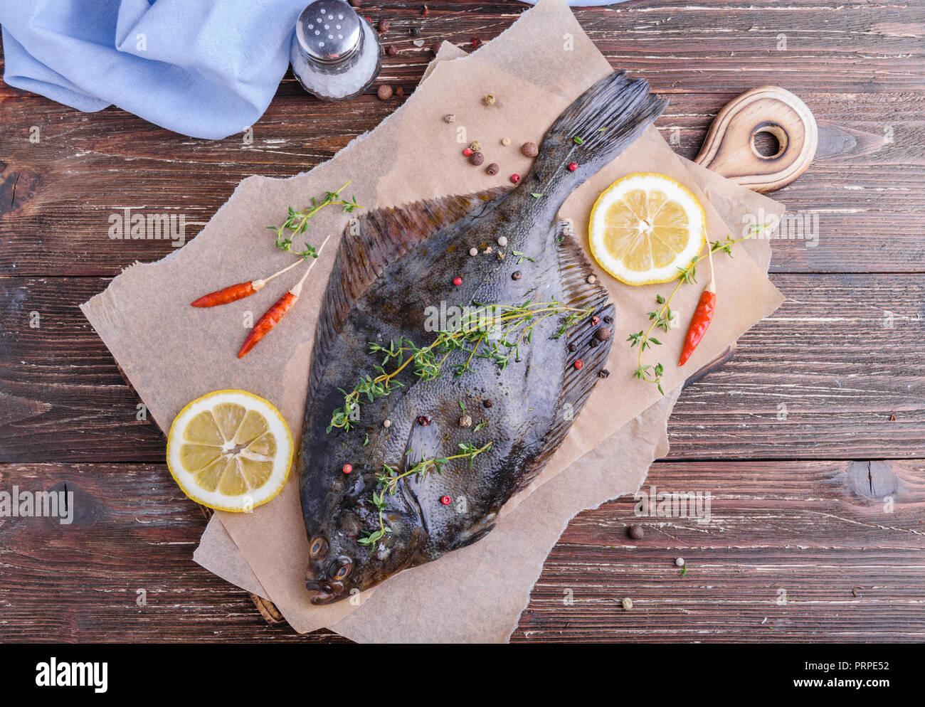 Raw flounder plaice fish (flatfish). Cooking process concept. Flounder fish with spices, lemon slices, thyme on parchment paper. Dark wooden table bac Stock Photo