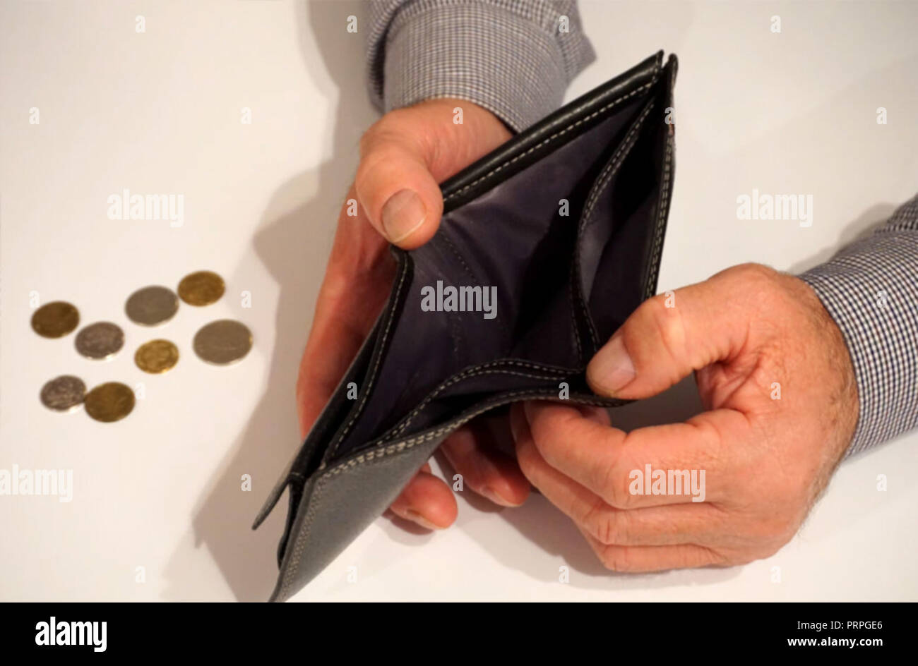 Black empty wallet in man hands with some coins in the background, on the white table. Poverty concept Stock Photo