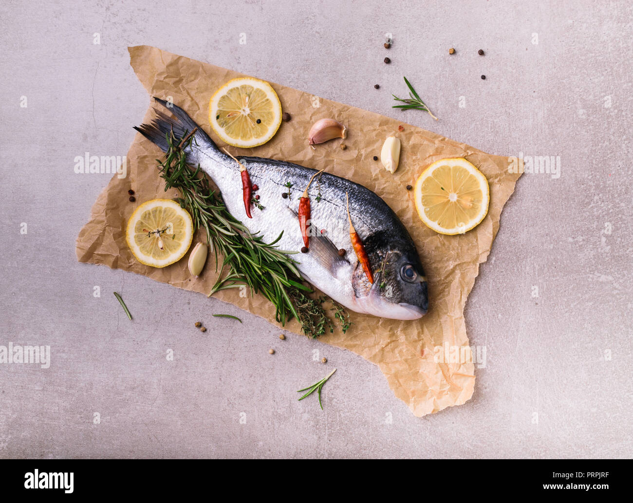 Fresh dorado fish. Dorado and cooking ingredients - rosemary, spices, lemon, garlic, thyme, herbs. Cooking concept. On light stone background. Top vie Stock Photo